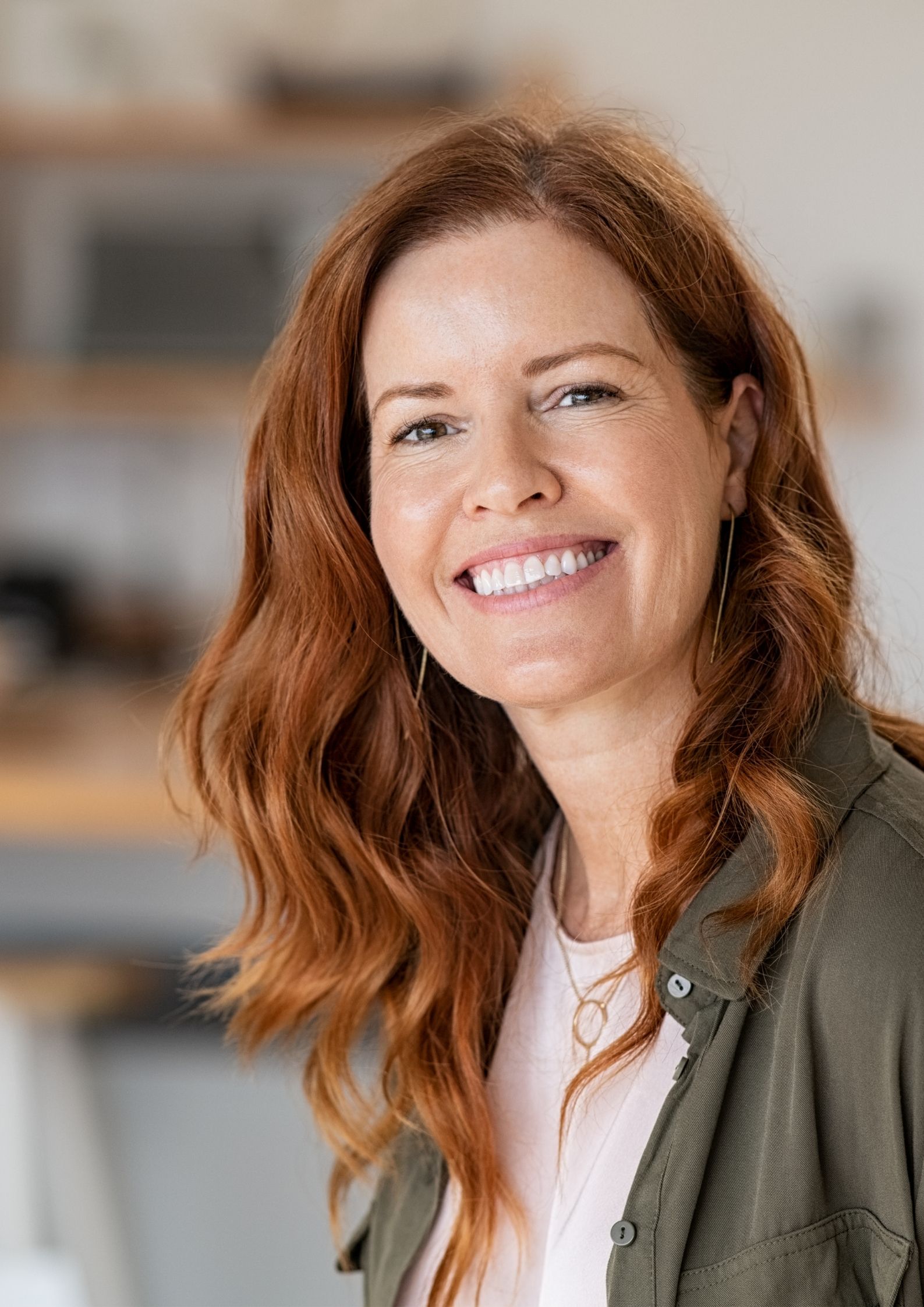 ptzykladowe zdjecie do zakladki kontakt pzredtsaiwajace osobe kobieta widoczna od polowy tlowia w gore piekny usmiech wyrazna twarz rozpuszcone rude wlosy tlo rozmyte